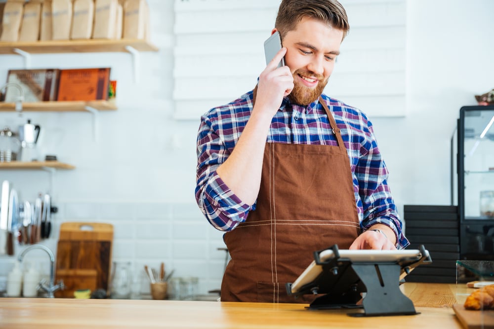 Smiling barista with taking order on cell phone and using tablet