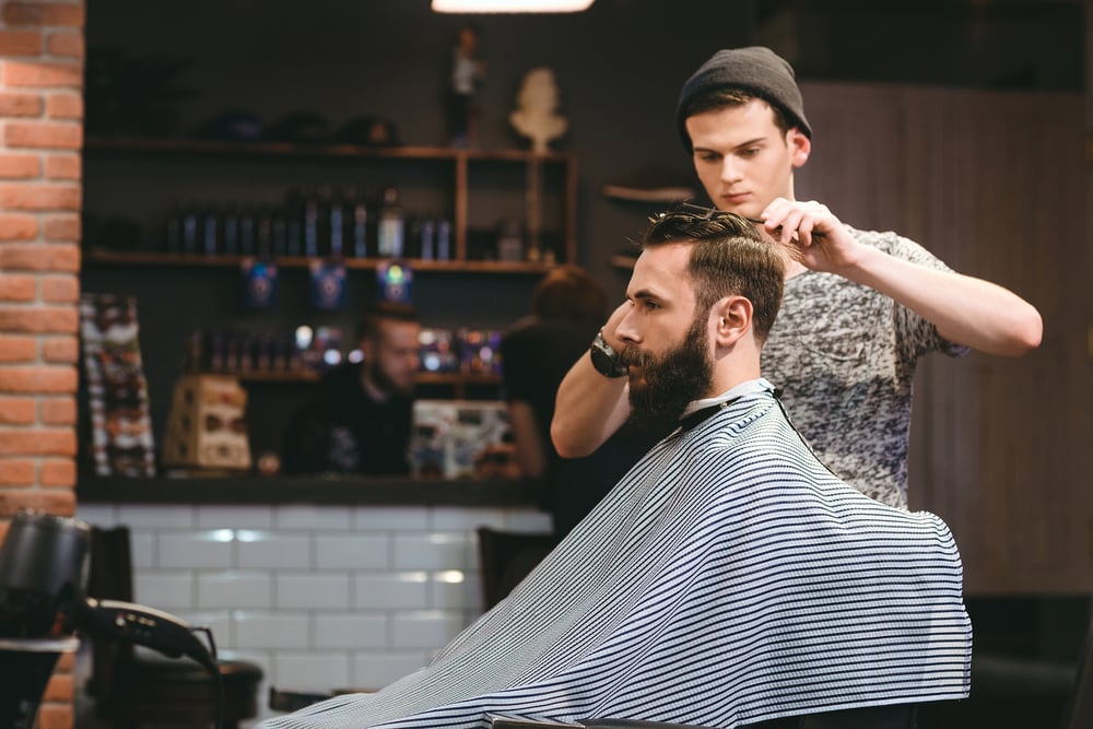 Barber trimming a bearded man in barbershop